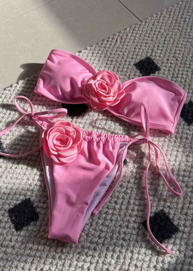 Pink bikini set with floral details on a textured surface