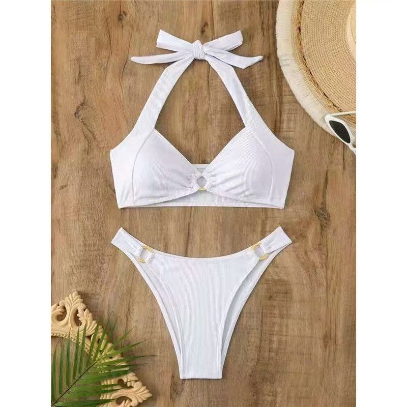 White bikini set on a wooden surface with a hat and sunglasses.