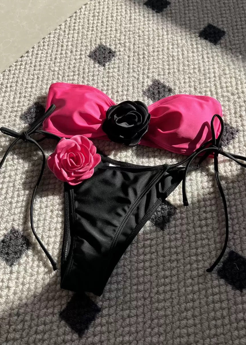 Black bikini bottom with pink floral top on a textured surface