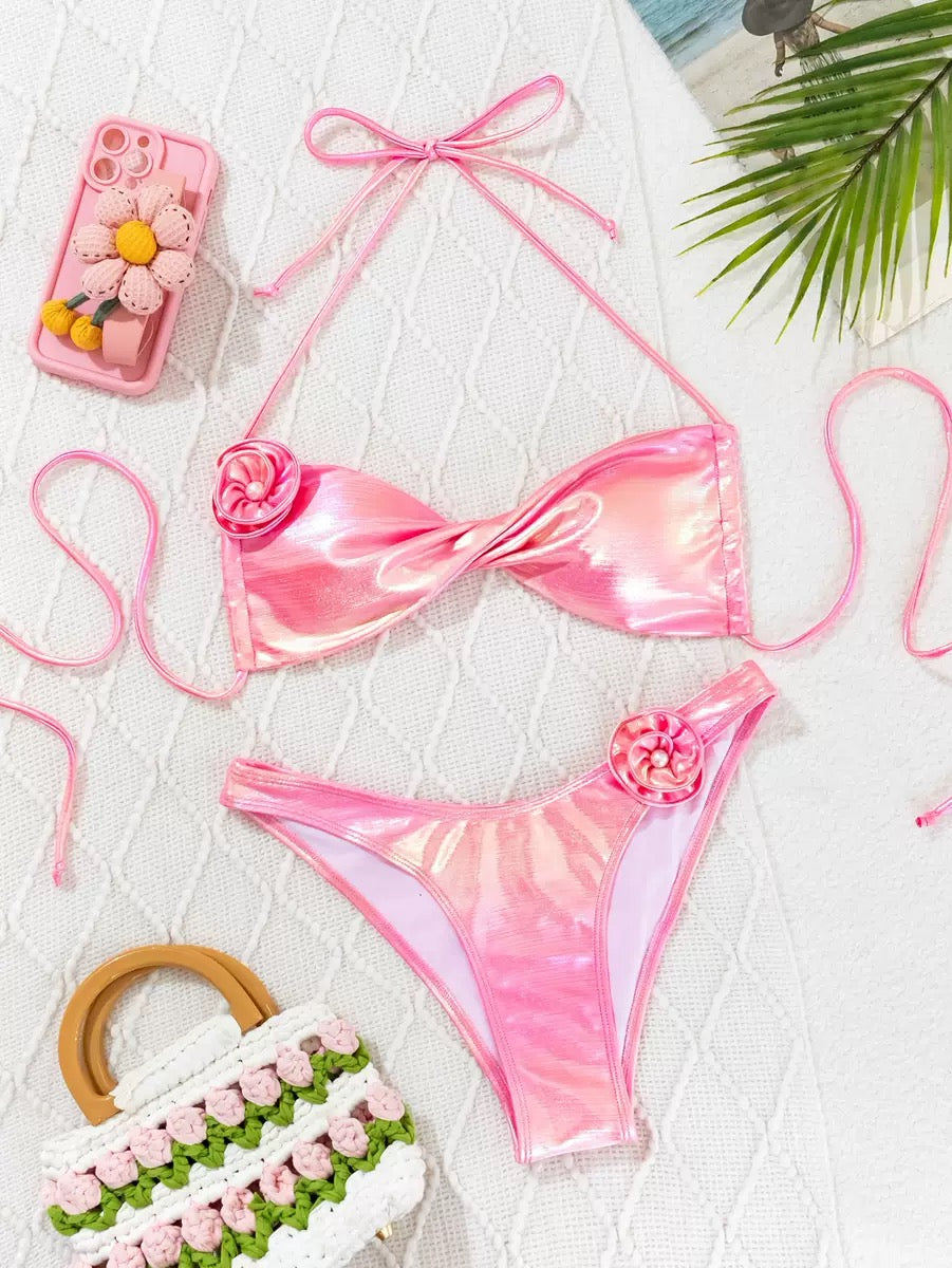 Pink bikini set with floral details on a white surface with decorative items.