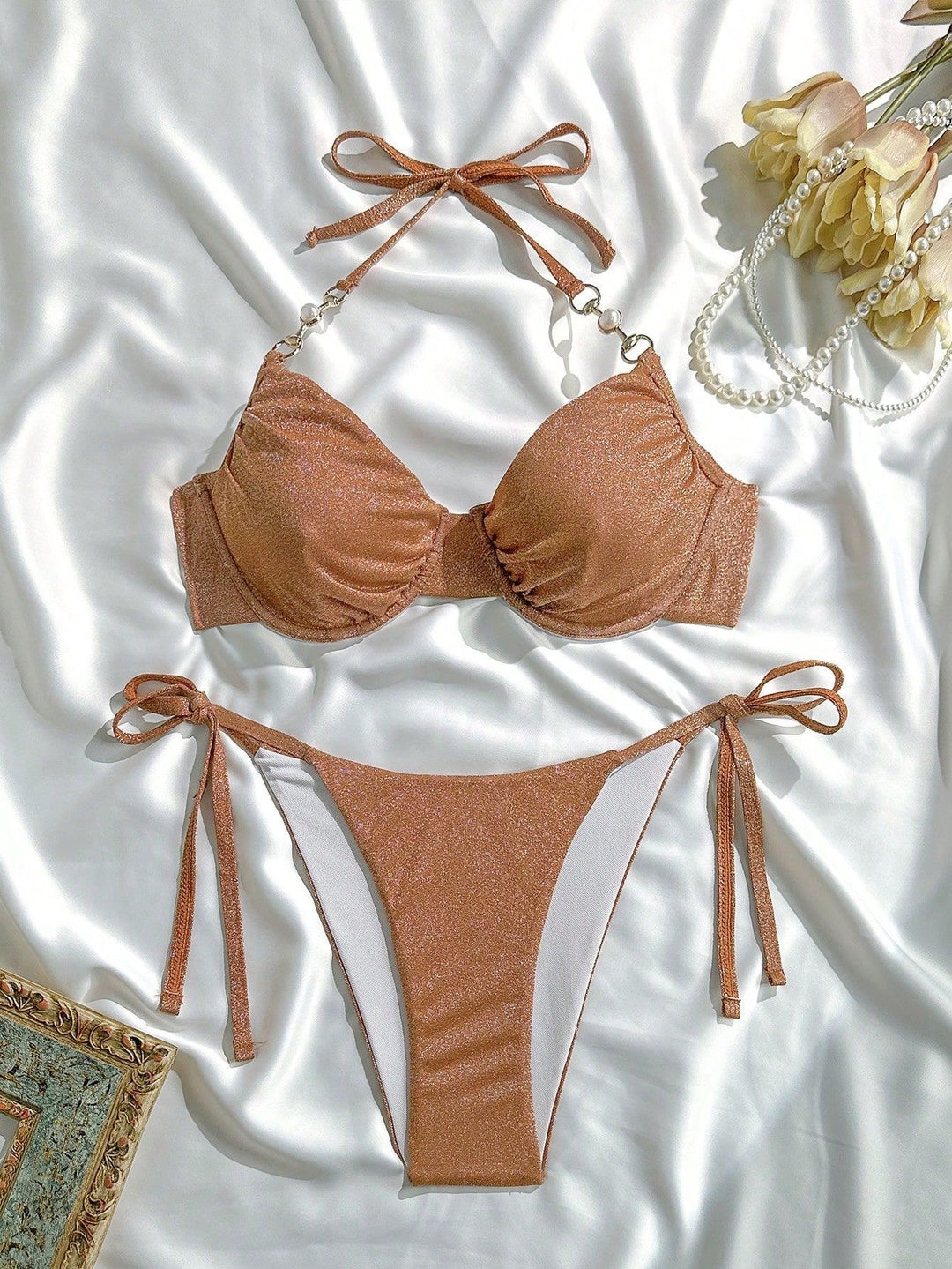Brown bikini set on a white fabric background with flowers and jewelry.
